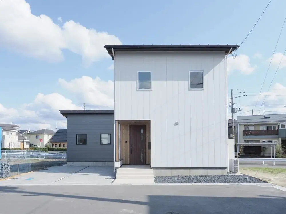 外観、母屋は白の縦太デザイン材×下屋は黒の横太デザイン材、玄関周りは米杉張りに、ステンロッドの筋交いがアクセント。<br>窓枠や玄関建具、ポスト等の色味までこだわった統一感あるシンプルデザイン。
